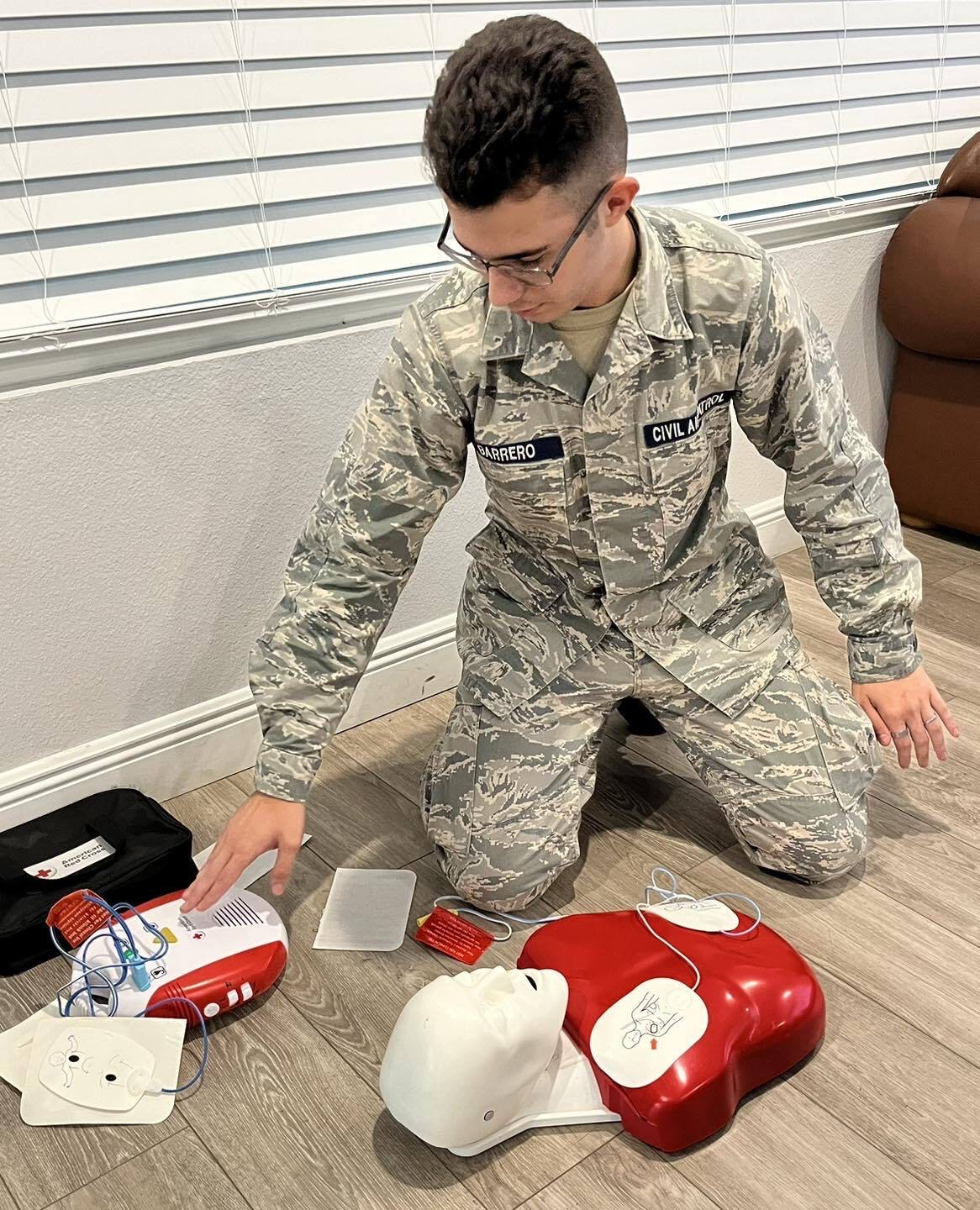 A cadet practicing with an automated external defibrillator and a CPR training manikin