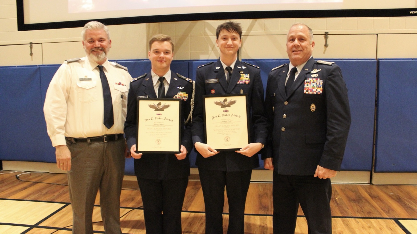 Two cadets holding framed award certificates alongside two squadron senior officers at an awards ceremony
