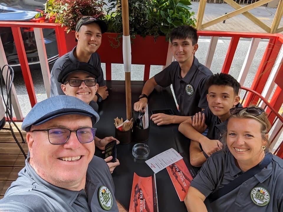 A senior member and cadets at a sidewalk cafe table during the squadron trip to France