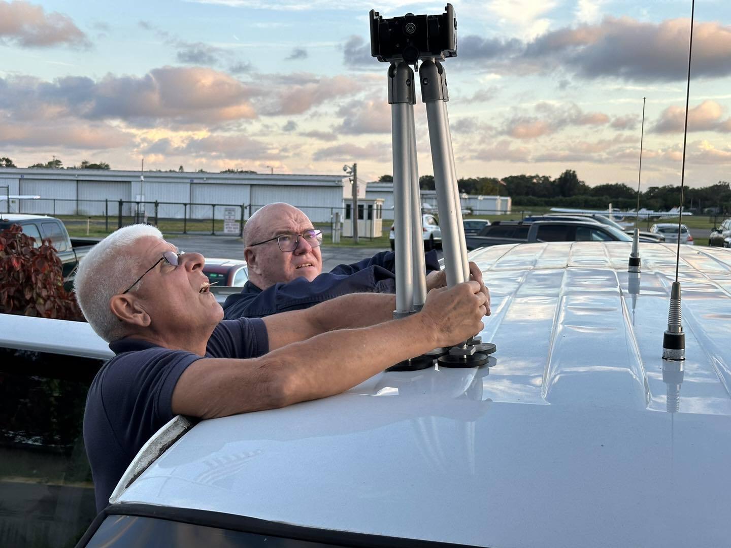 Two adult senior members fitting an antenna mast to the roof of the squadron communications van at dusk